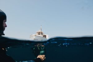 A diver underwater with a yacht on the surface, showcasing split-level photography. Ideal for marine adventure themes.